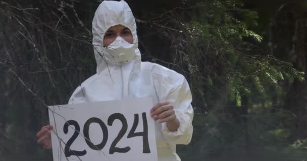 新年份2024年 白纸版与题词 2024年 身穿白色防疫服的医生手里拿着一面纸板横幅 在树林里 是的高质量的照片 — 图库视频影像