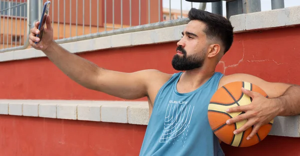 Genç bir çocuk basketbol oynadıktan sonra cep telefonuyla fotoğraf çekiyor.