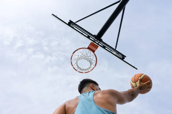 Şehir basketbol sahasında basketbol oynayan mavi tişörtlü bir çocuk.