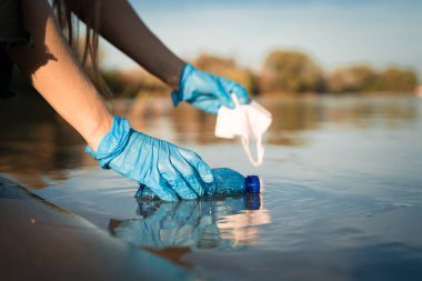 Eller nehirden çöp ve çöp topluyor, deniz suyu, plastik şişe ve maske topluyor. Plastik kirliliği kavramı. Çevresel sorun kavramı. Sorun plastik şişeler ve mikro plastikler.