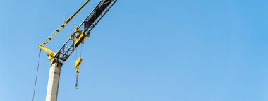Sarı vinç çalışıyor ve ağırlık kaldırıyor. İnşaat konsepti. İnşaat ve el işleri. Açık mavi arkaplan. nötr gökyüzü.