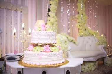 Pembe çiçekli beyaz düğün pastası.