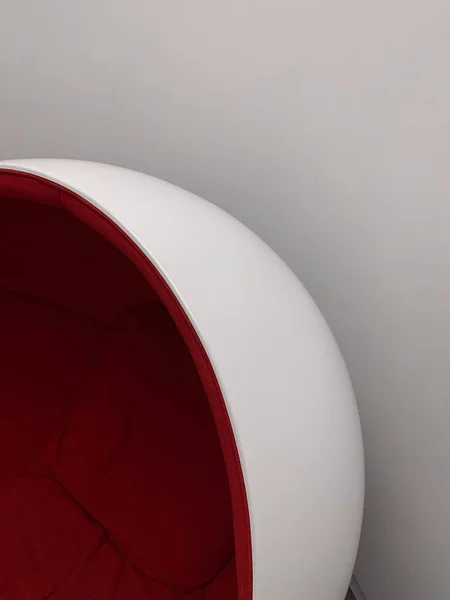 Red accent on a white armchair, against white wall. future.