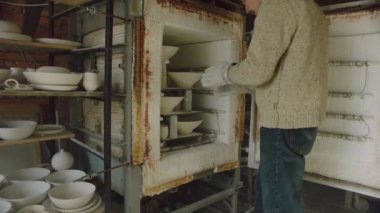 Man Potter fırından seramik çıkarıyor.
