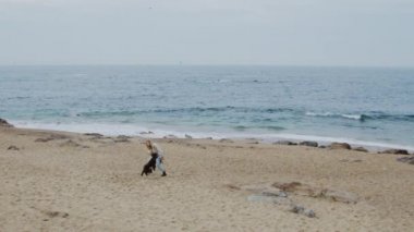 Kadın sahilde köpekle oynuyor.