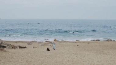 Kadın köpekle sahilde yürüyor.