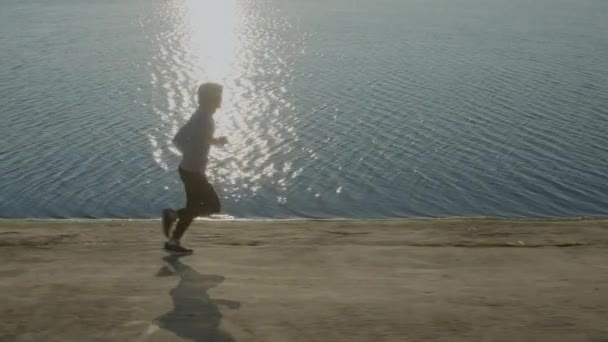Silny człowiek biegnie w pobliżu jeziora. — Wideo stockowe