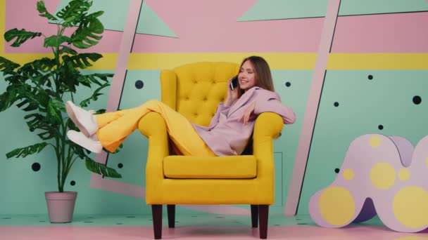 Vrouw in gele fauteuil is praten telefoon — Stockvideo