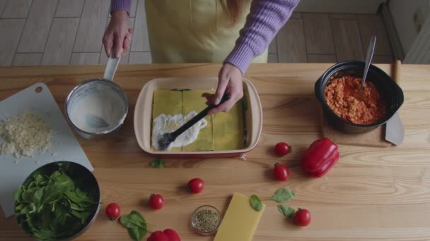 Женщина кладёт соус на лазанью — стоковое видео