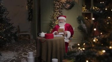 Mutlu Noel Baba çocukların ve yetişkinlerin mektuplarını okuyor, ve sonra kameraya bakıp gülümsüyor, Noel geliyor, Ağır çekim.