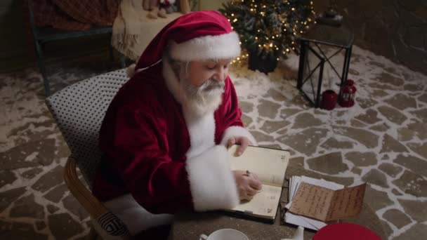 圣诞老人在他的住宅里愉快地工作着 在他的计划中列出了礼物的清单 处理收到的信 圣诞精神 慢动作 — 图库视频影像