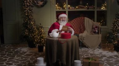 Mutlu Noel Baba evinin arka bahçesinde oturuyor, Kuzey Kutbu 'nda, mektup okuyor, ve sonra kameraya bakıyor ve gülümsüyor, Noel ruhu, ağır çekim.
