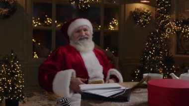 Mutlu Noel Baba, gri sakallı yaşlı adam, masada oturuyor ve kameraya gülümsüyor, bayram atmosferini paylaşıyor, Noel geliyor, Ağır çekim.