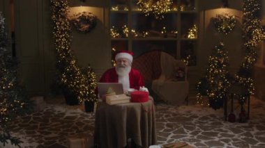 Meşgul Noel Baba gece geç saatlerde arka bahçesinde çalışıyor, e-postaları kontrol etmek için dizüstü bilgisayar kullanıyor, kış tatili sezonuna hazırlanıyor,.
