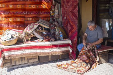 Bergama, İzmir, Türkiye - 10.2022: Geleneksel halı dikme dükkanı önünde el yapımı halı ören adam, geleneksel halı dikme adamı