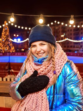 Eşarplı, şapkalı, ceketli, eldivenli, açık hava pistinde gülümseyen beyaz bir kadın. Yeni yıl, eğlence, kış konsepti 