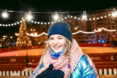 Eşarplı, şapkalı, ceketli, eldivenli, açık hava pistinde gülümseyen beyaz bir kadın. Yeni yıl, eğlence, kış konsepti 