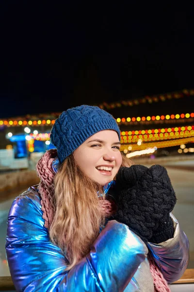 Eşarplı, şapkalı, ceketli, eldivenli, açık hava pistinde gülümseyen beyaz bir kadın. Yeni yıl, eğlence, kış konsepti 