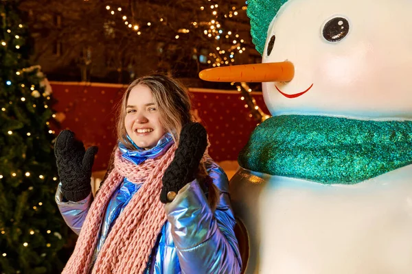 Eşarplı, şapkalı, ceketli, kardan adamın eldivenli mutlu beyaz kadın. Yeni yıl, eğlence, kış konsepti