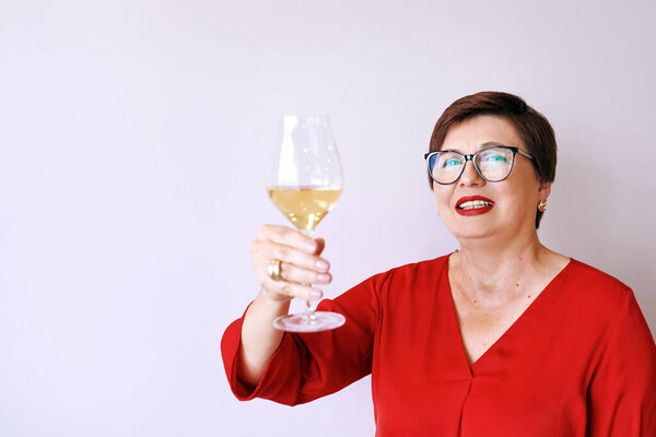 stylish mature senior woman in red blouse with glass of white wine celebrating new year. Fun, party, style, lifestyle, alcohol, celebration concept