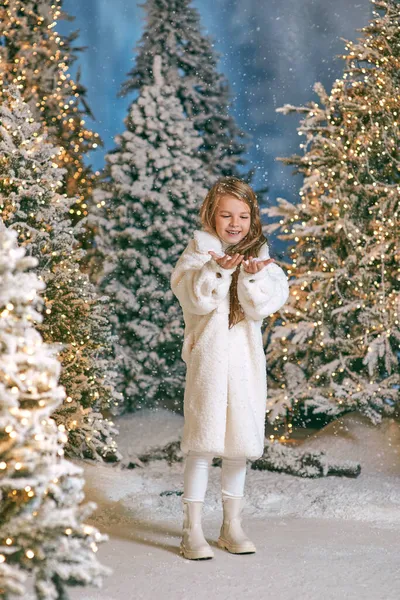 Beyaz eko kürklü şirin sarışın kız kışın yılbaşı ormanında ışıklarla yürüyor. Yeni yıl, peri masalı konsepti