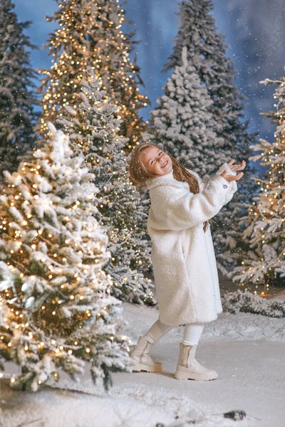 Beyaz eko kürklü şirin sarışın kız kışın yılbaşı ormanında ışıklarla yürüyor. Yeni yıl, peri masalı konsepti