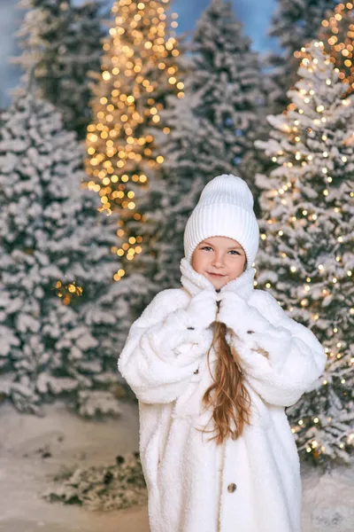 Beyaz eko kürklü, şapkalı ve eldivenli, kışın ormanda yürüyen beyaz saçlı sarışın kız. Yeni yıl, peri masalı, moda konsepti