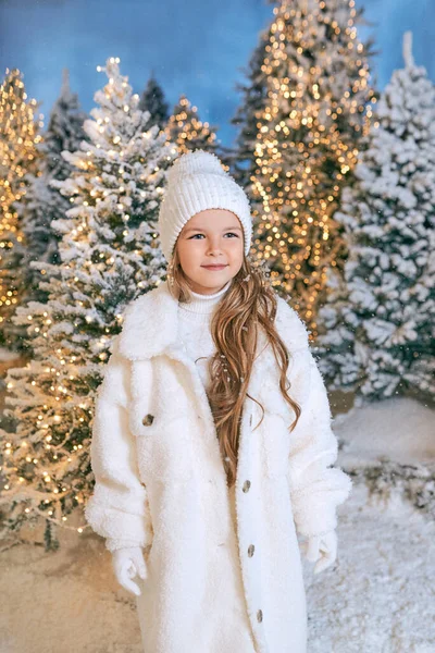 Beyaz eko kürklü, şapkalı ve eldivenli, kışın ormanda yürüyen beyaz saçlı sarışın kız. Yeni yıl, peri masalı, moda konsepti