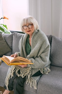 Kanepede oturmuş evde kitap okuyan eski moda son sınıf öğrencisi kadın. Eğitim, olgun, boş zaman kavramı