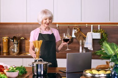 Son sınıf neşeli kadın modern mutfakta dizüstü bilgisayarla yemek pişiriyor. Gıda, eğitim, yaşam tarzı konsepti 