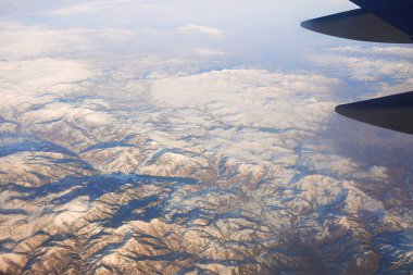 View to the wing of airplane in the sky and snowy mountains. Travel and transportation concept