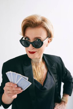 Siyah smokinli ve kumarhanede güneş gözlüklü olgun bir kadın. Kumar, moda, poker yüzü, floş royal, hobi konsepti.