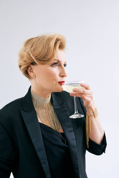 mature stylish elegant woman in tuxedo with glass of sparkling wine. Party, celebration, anti age concept 