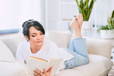 Kanepede kitap okuyan güzel bir kadın. Boş zaman, eğitim, kişisel gelişim kavramı.