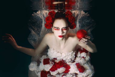Woman in dress made of white and red roses underwater. Fairy tale, art, fashion concept
