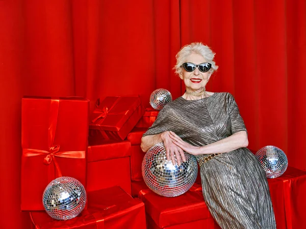 Senior stylish elegant woman with disco ball wine on red background. Party, fashion, celebration, anti age concept