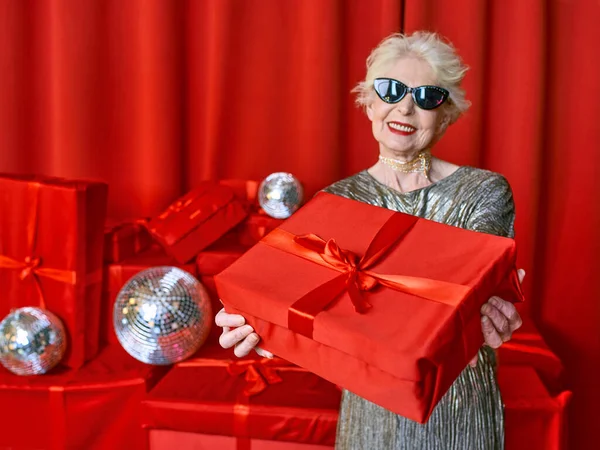 senior stylish woman with presents on red background. Party, fashion, celebration, anti age concept