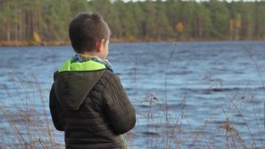 Çocuk gölün kıyısında tek başına duruyor.