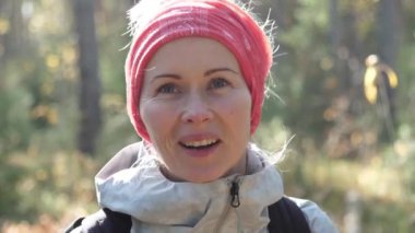 Güzel beyaz bir kadın kafasında atkıyla ormanda tek başına kameraya gülümsüyor.