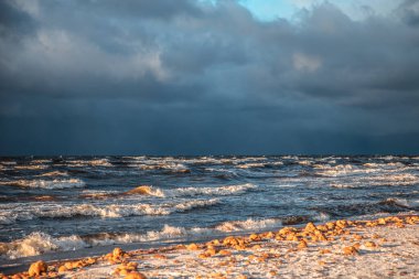 Deniz dalgalarında gün ışığı parlar. Rüzgar dalgaları kıyıya vurur. Kışın, toprak seti taşlarla kaplıdır.