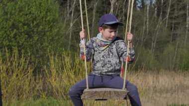 A child on a big swing. The boy is sitting on a wooden swing
