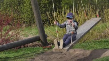 Büyük bir salıncakta sallanan bir çocuk. Çocuk ahşap salıncakta oturuyor.