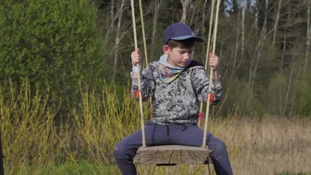一个大秋千上的孩子那男孩正坐在一个木制的秋千上 — 图库视频影像
