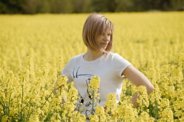 Çiçekli tecavüz tarlasında bir kadın. Kolza çiçekleri sarıdan güneşe. Çiftçi yağ tohumu tecavüzü yetiştiriyor