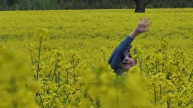 Çocuk kolza tohumu tarlasında oynuyordu. Sarı tarımsal tecavüz. Çocuk kanola sevdiğini gösteren bir parmak gösteriyor.