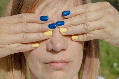 Ukrayna bayrağı renkli tırnakları olan bir kadın. Kadının gözlerine avuç içi yapışmış.