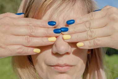 Ukrayna bayrağı renkli tırnakları olan bir kadın. Kadının gözlerine avuç içi yapışmış.