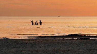 Silhouettes of people by the sea at sunset. The family swims in the sea