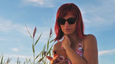 Woman with mobile phone on seashore at sunset. Beautiful woman on the beach under the hot sun