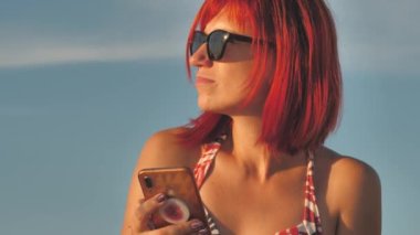 Woman with mobile phone on seashore at sunset. Beautiful woman on the beach under the hot sun